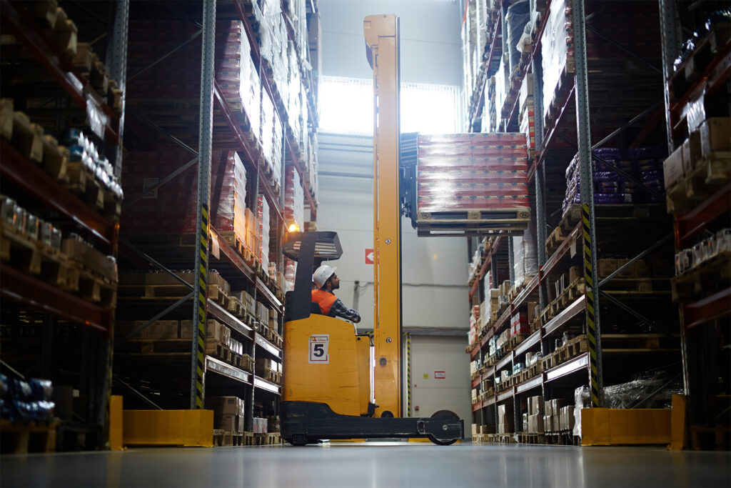 Side view portrait of warehouse worker using a reach fork truck to load pallet with boxes on tall rack
