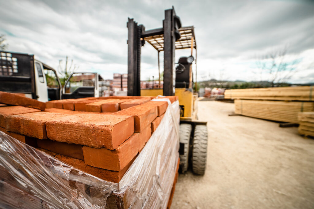 a forklift holding pallets of bricks on a construction site
