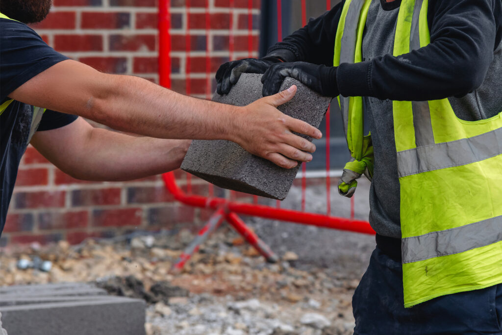 manual handling on a construction site as two workers pass a concrete block between them