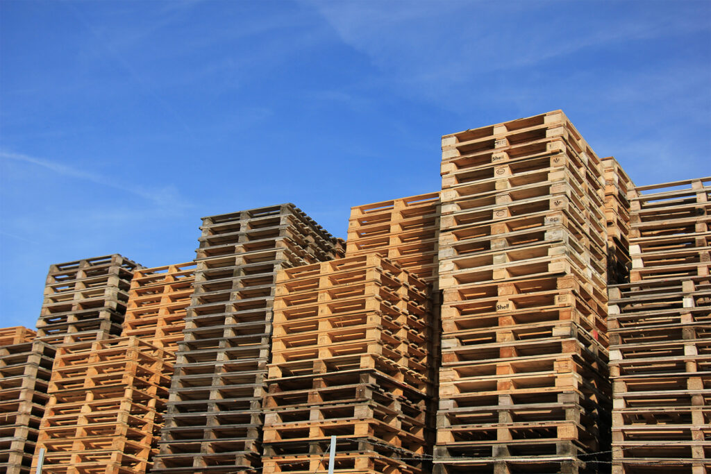stacks of standard wooden pallet sizes for the UK market against a blue sky
